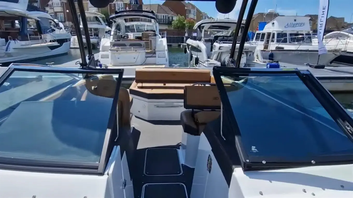 Interior of a yacht with panoramic windows, showcasing a wooden seating area, cockpit controls, and moored boats in the background.